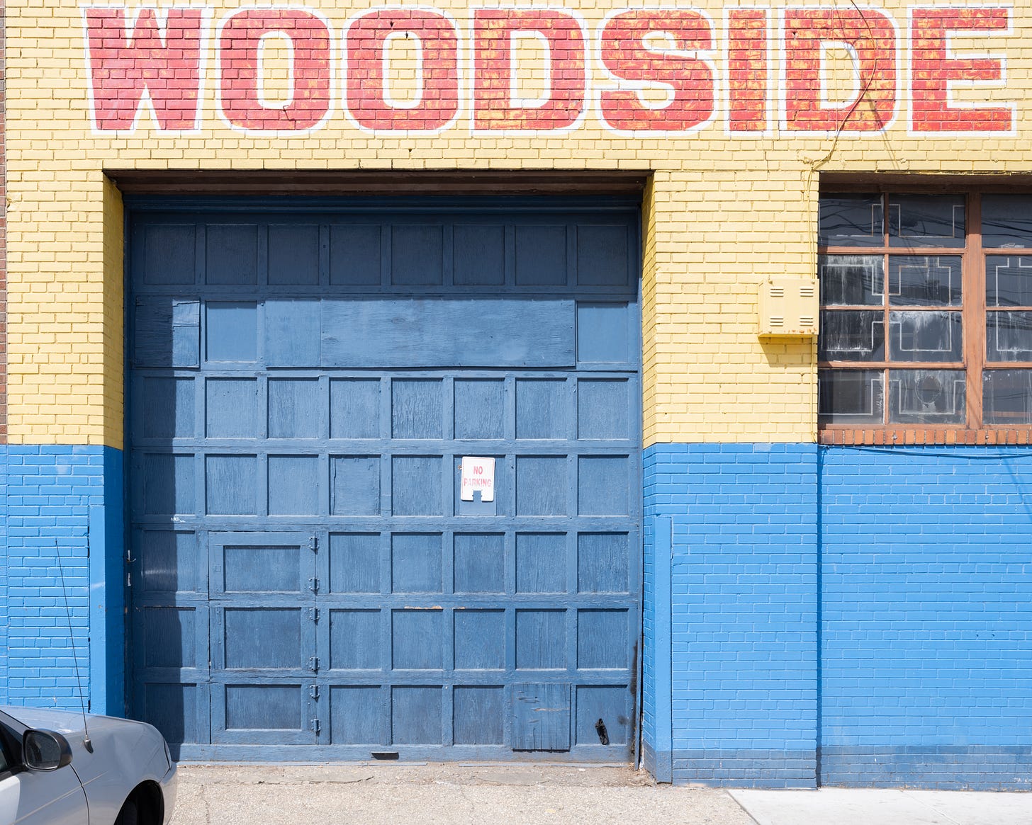 WOODSIDE written in big red block letters on yellow wall over blue painted garage door
