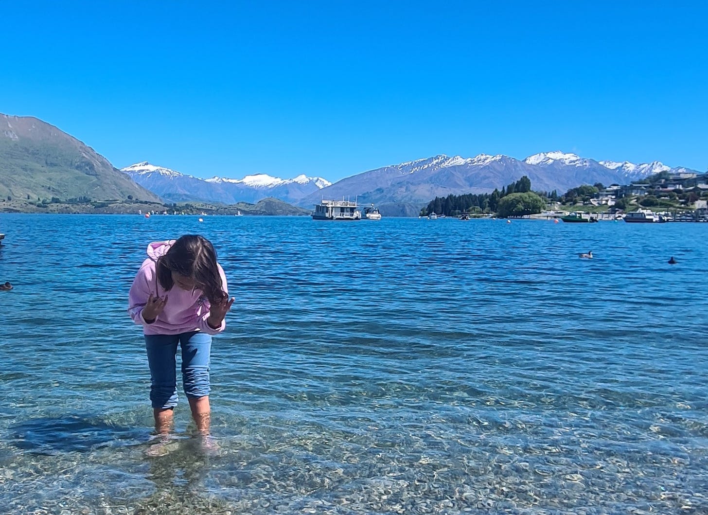 photo of a child paddling in lake wanaka with snow covered mountains in the backgroun