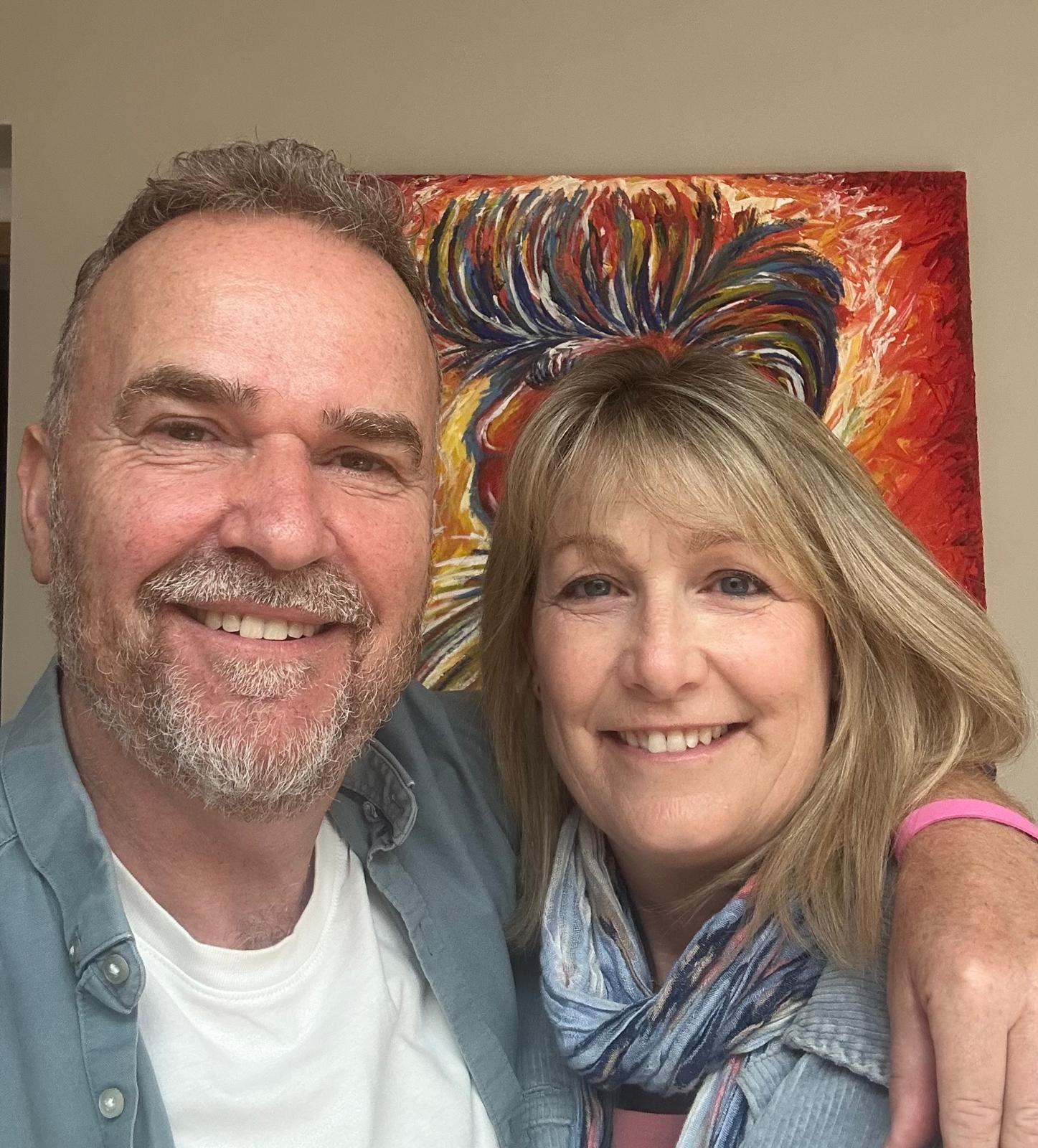 middle aged man and woman with arms round each other, smiling, wearing trans colours