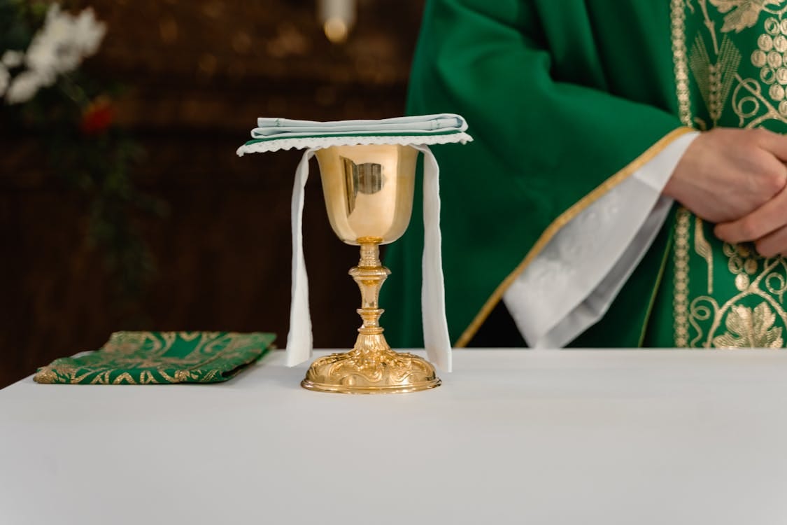 Free Golden Chalice on Table Beside a Priest in Green Chasuble Stock Photo