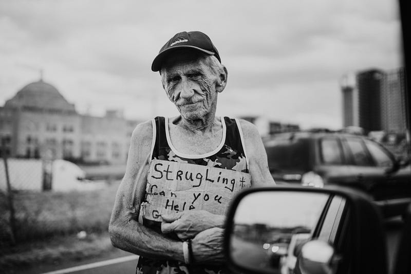 Black and white photo of a homeless man carrying a sign.