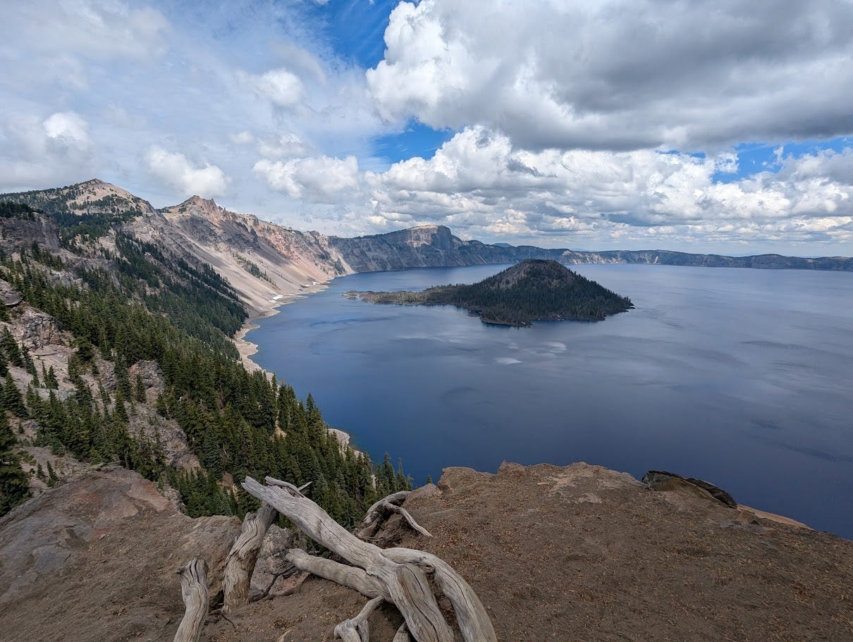 A blue lake at the top of a mountain with a small island in the center of the lake, fluffy clouds in the sky