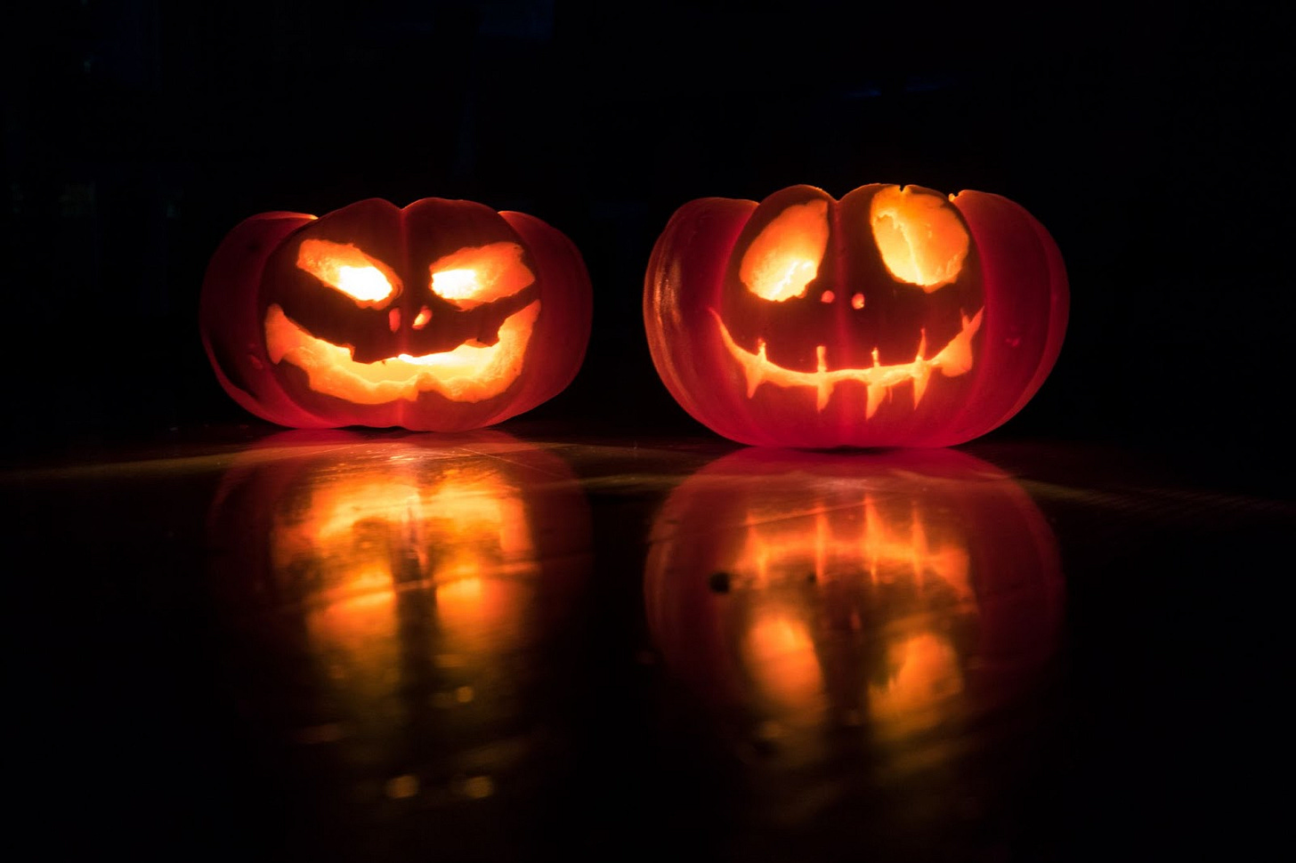 Two jack-o-lanterns on a black background and a reflective black floor. Two jack-o-lanterns on a black background and a reflective black floor.