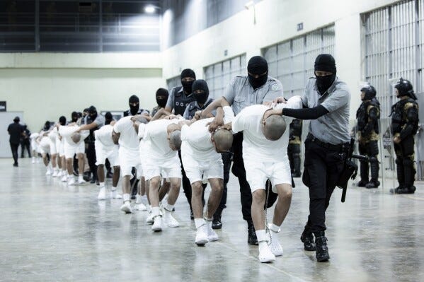 En esta fotografía proporcionada por la oficina de prensa de la presidencia de El Salvador, guardias penitenciarios trasladan a presuntos pandilleros venezolanos, deportados de Estados Unidos, al Centro de Confinamiento del Terrorismo (CECOT), en Tecoluca, El Salvador, el domingo 16 de marzo de 2025. (Oficina de prensa de la presidencia de El Salvador vía AP)