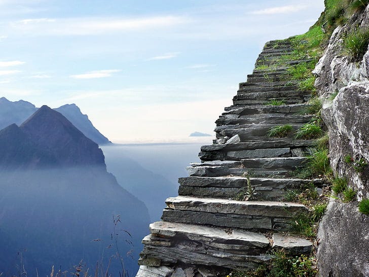 A stone staircase cut into the side of the mountain, overlooking an expanse of water and blue-grey mountains. 