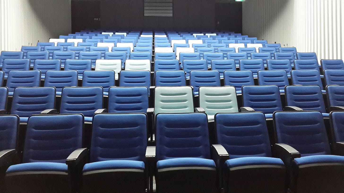 An auditorium with green and blue folding seats