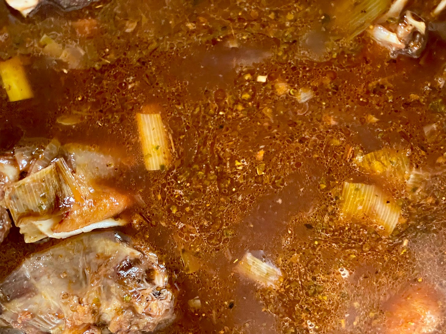 A close-up of a simmering pot of sauce with visible roasted vegetable pieces, leeks, and a glossy surface. A close-up of a simmering pot of sauce with visible roasted vegetable pieces, leeks, and a glossy surface.