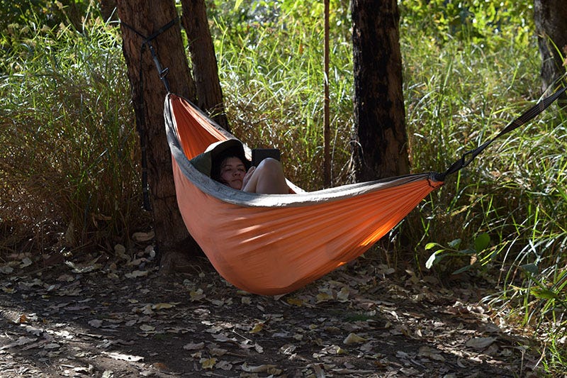 A woman sits in an orange hammock, reading a Kindle.