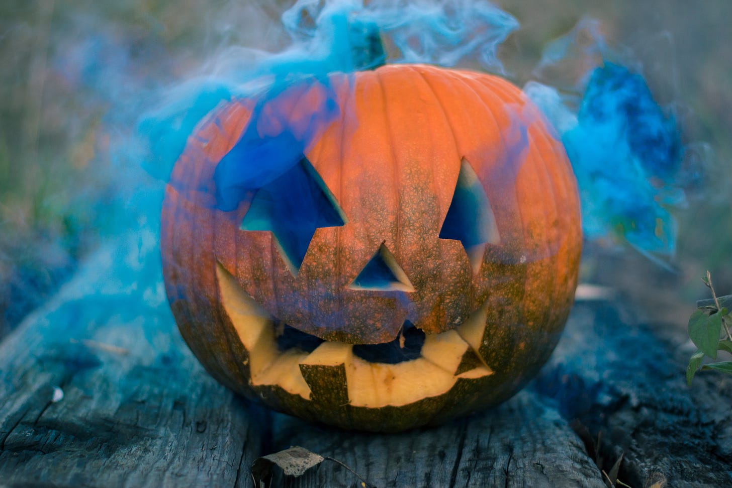 An orange pumpkin sits on a picnic bench with blue smoke emanating from its eyes 