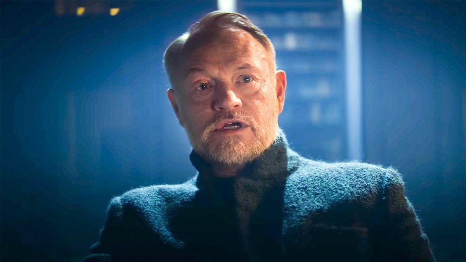 Still of Jared Harris as Hari Seldon in Foundation. Scene in Medium Close Up in a darkened library, speaking to someone just past the camera.
