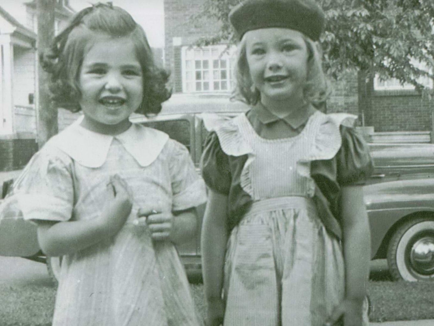 Two little girls standing on a sidewalk smiling