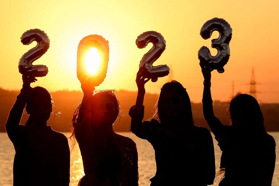 Four women are silhouetted against the setting sun as they hold up number-shaped balloons spelling out "2023."
