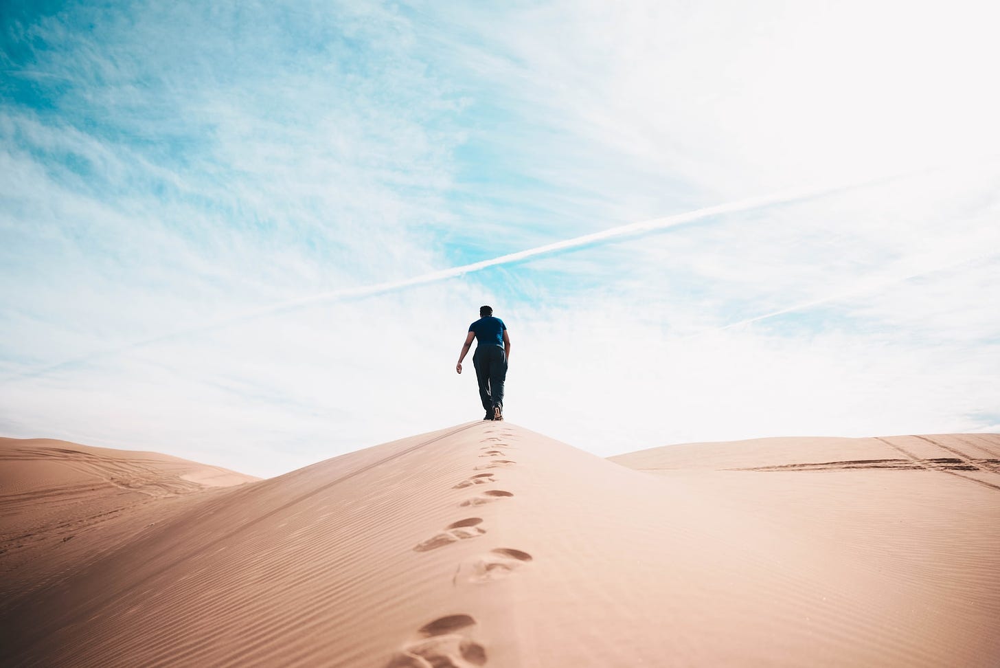 A person walks up a hill in a desert leaving footprints behind with each step.