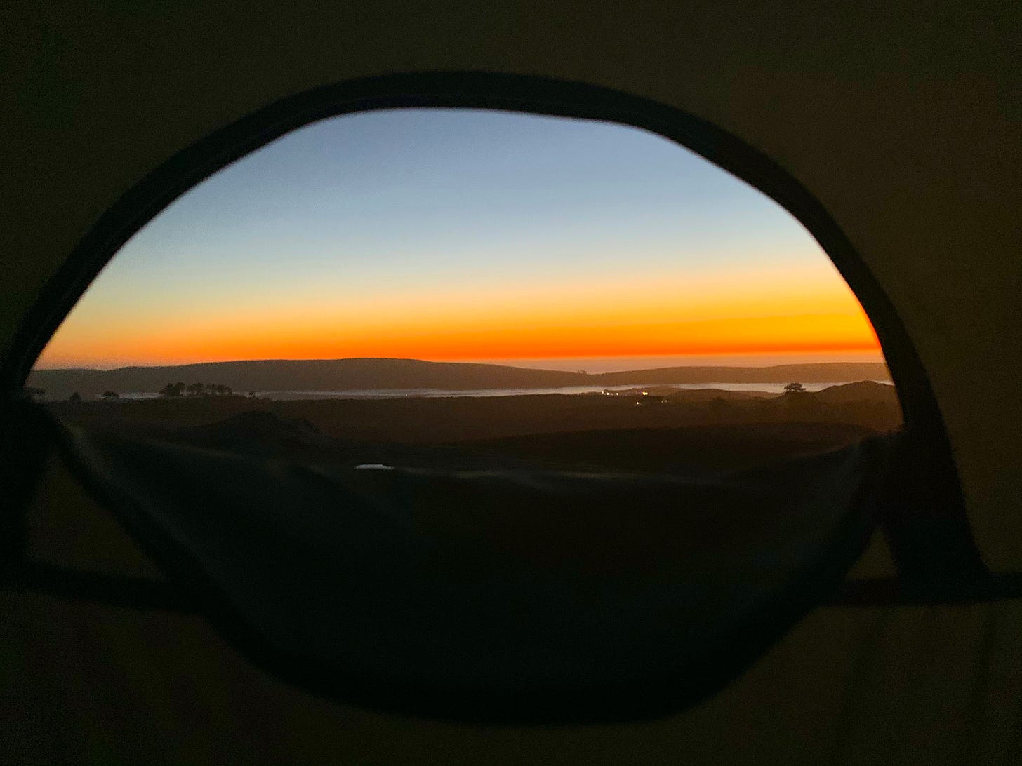 A sunset over the bay captured through a small dome-shaped tent window.