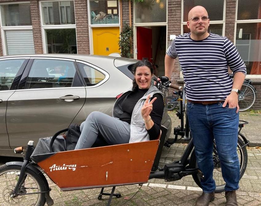 Nicolai sat in the front box of a cargobike. James is posing next to her. 