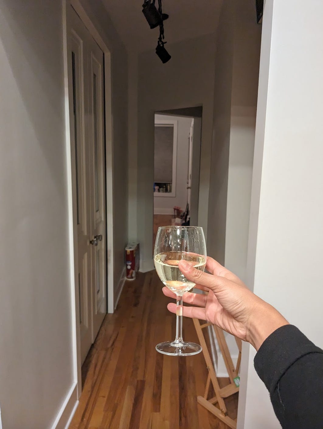 Nathalie's hand hold a wine cup of champagne towards a long hallway