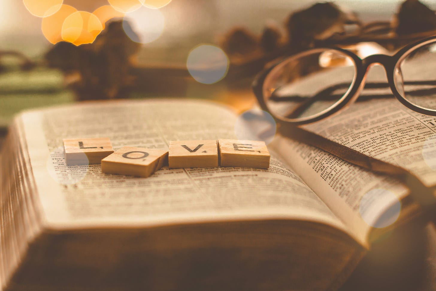 Image of a Holy Bible opened with a pair of glasses on top and four wooden tiles spelling out LOVE.