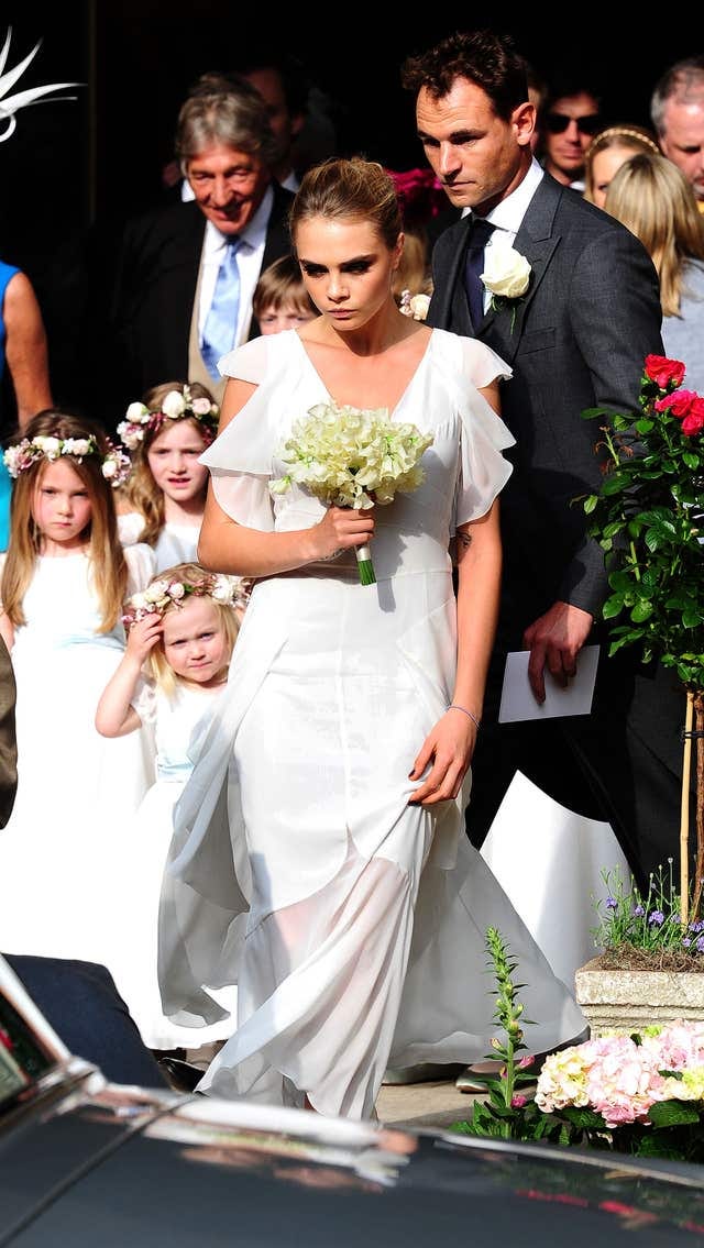 Cara Delevingne in white dress holding flowers at the wedding of her sister Poppy Delevingne and James Cook