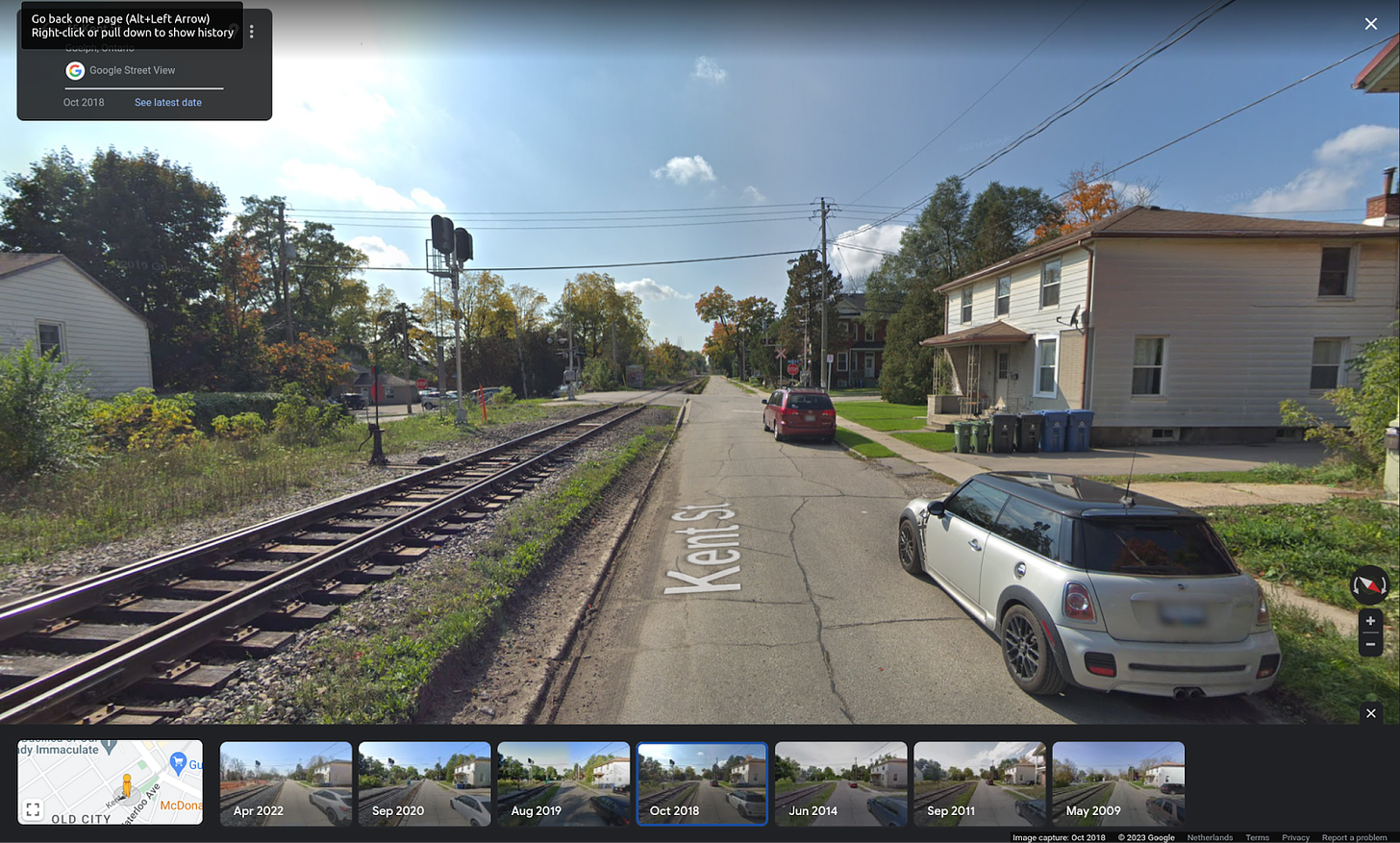 A residential street with houses on one side and railway tracks where you might find a sidewalk on the other side.