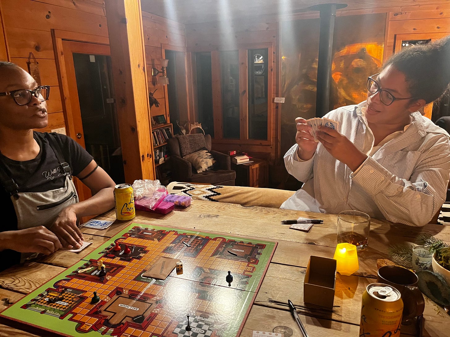 Nafissa and Jackie play Clue on a wooden table inside the wood cabin.