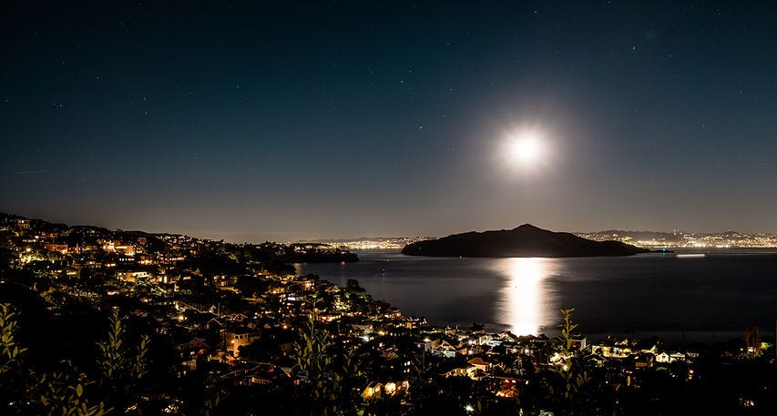Image of Sausalito bay in the evening with the full moon, looking over the neighbourhood lights.