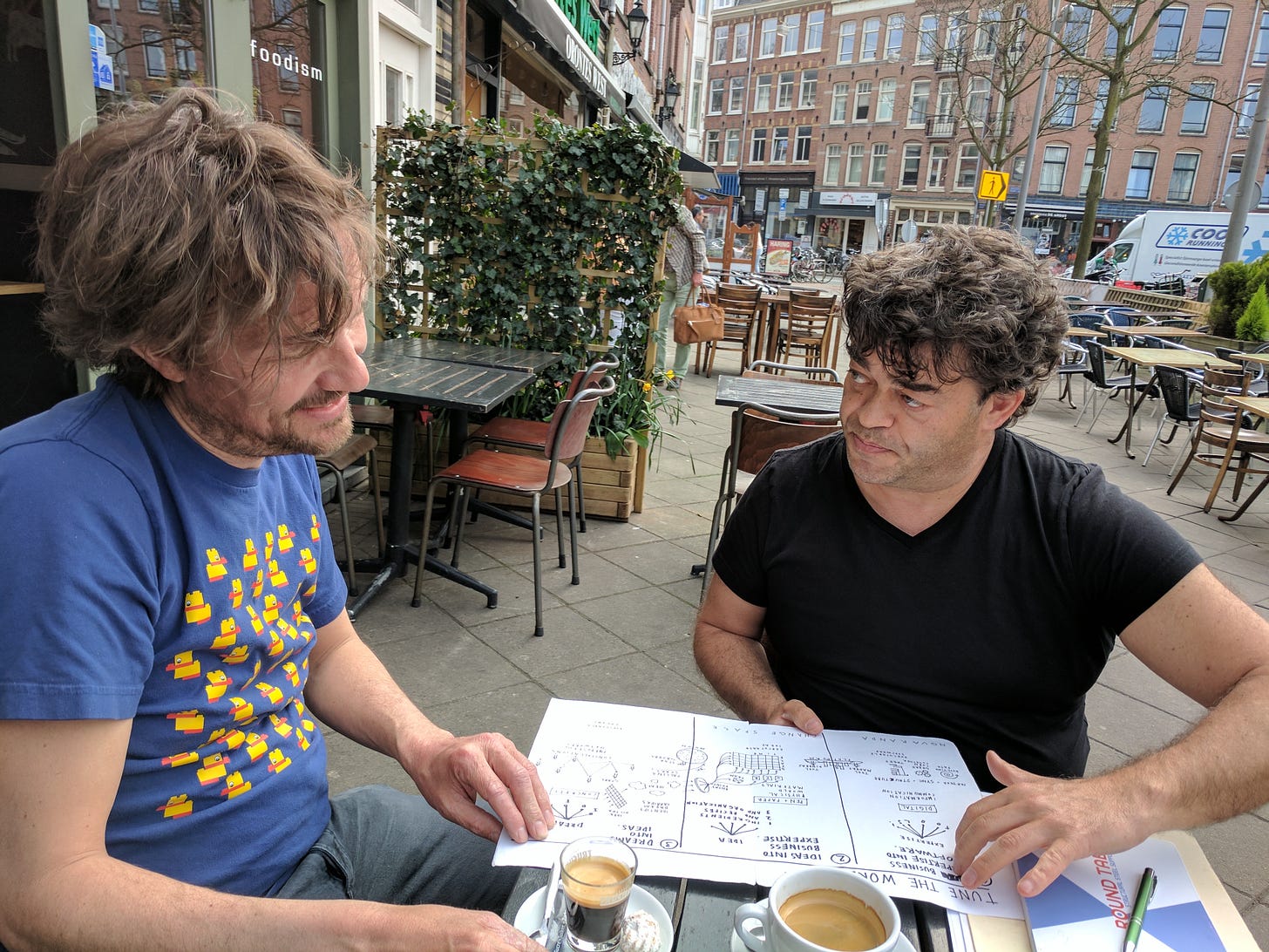 Two guys at an outdoor cafe reviewing a diagram