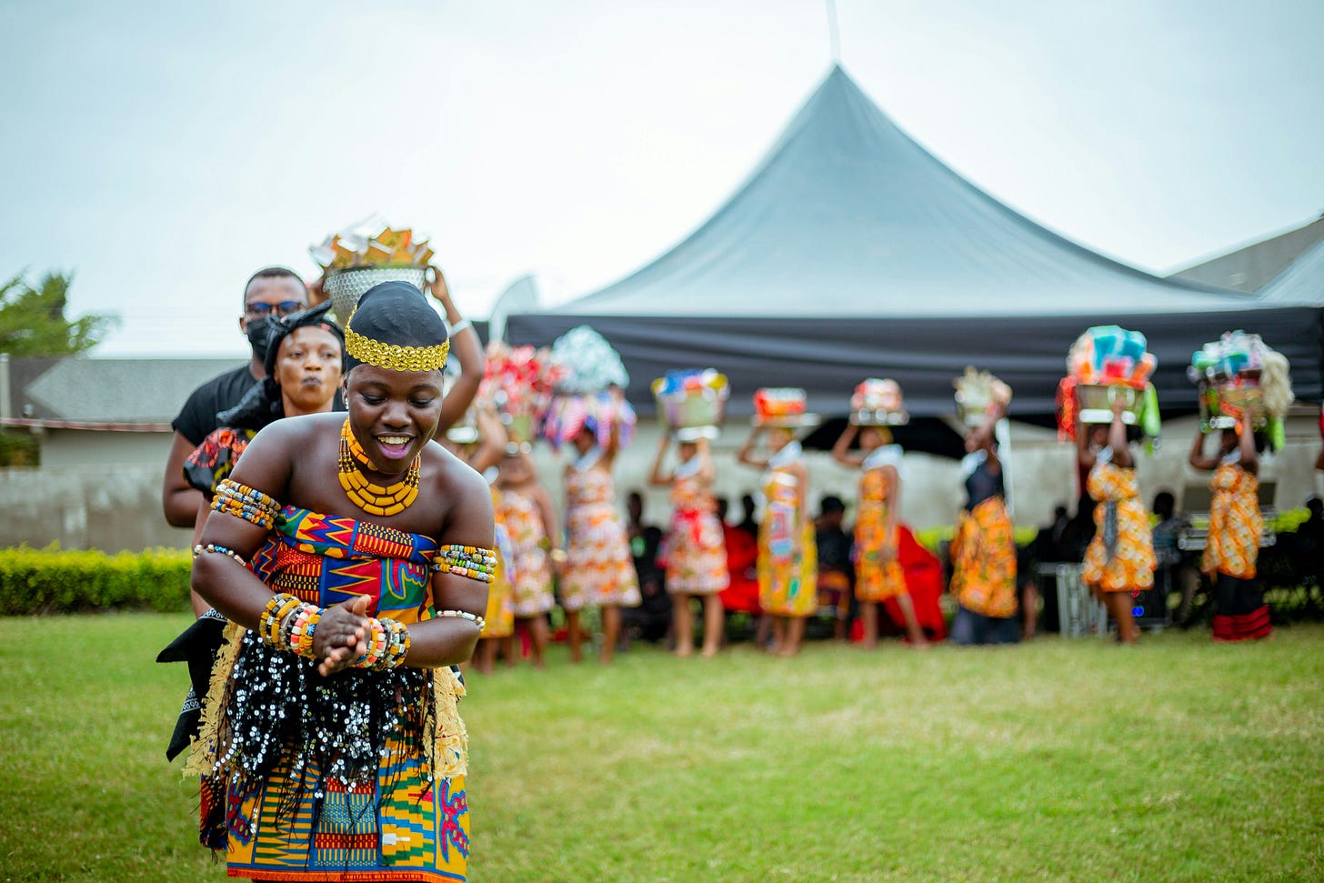 A smiling woman in traditional dress leads a conga line during an outdoor celebration in Accra, Ghana © Ransford Quaye 2022