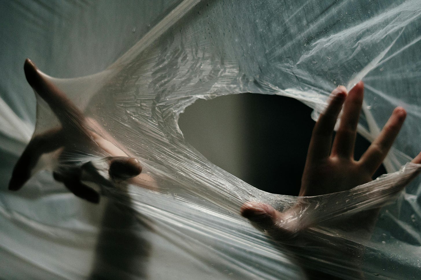 This  picture is of a pair of hands behind a transparent sheet of what seems like nylon material. Whilst one hand has it's index finder attempting to push through the nylon, the other hand has successfuly pierced it and is poking through the big oval shaped hole in it. This picture could be interpreted as someone trapped behind the nylon sheet and is trying to fight their way out and at the same time poking a hole to gasp for air.