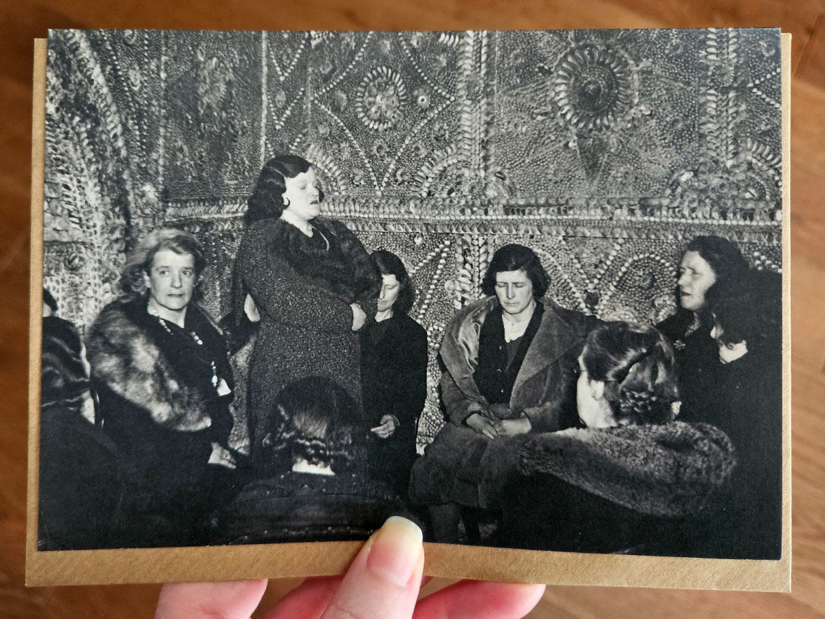 A hand holding a gift card featuringa  black and white image of women sitting and standing in a circle