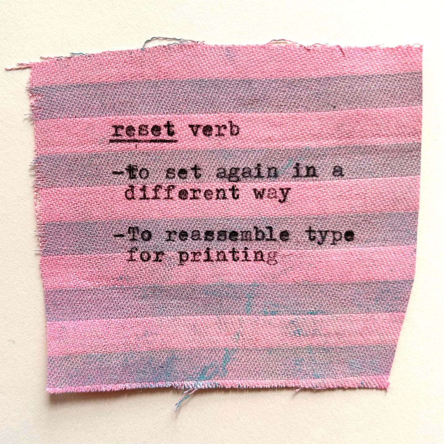 A scrap of shirt fabric, painted pink and typewritten with: “reset, verb: To set again in a different way - To reassemble type for printing