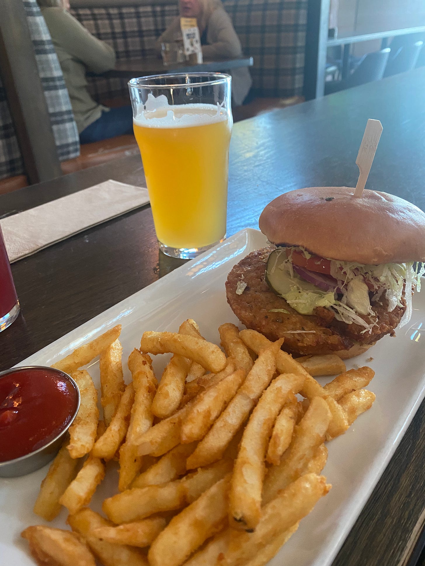 A rectangular plate with a veggie burger and beer-battered fries, with a side of ketchup. A glass of beer is in the background.