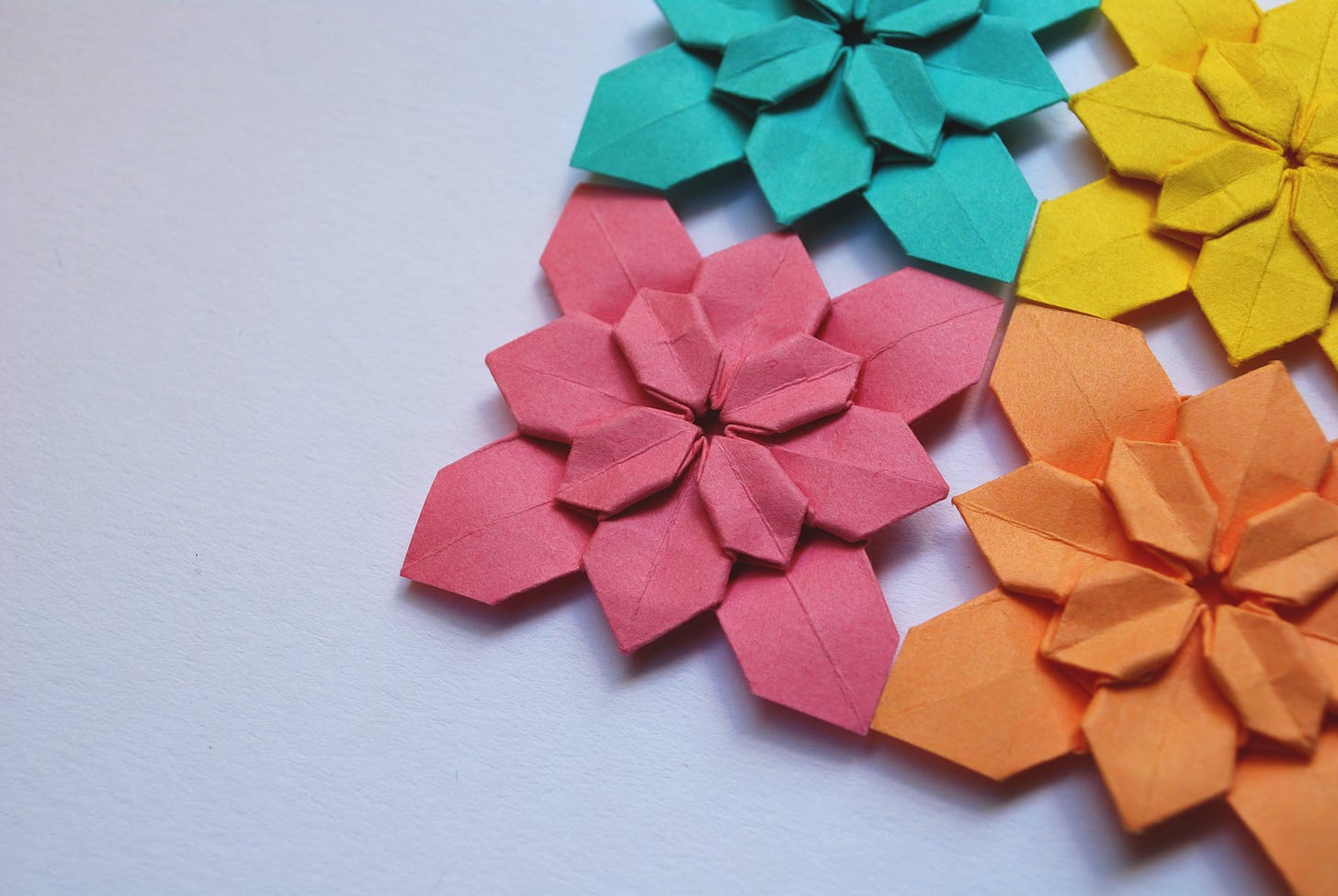 An off-center shot of four origami flowers or stars in different colors: pink, orange, yellow, and teal. 