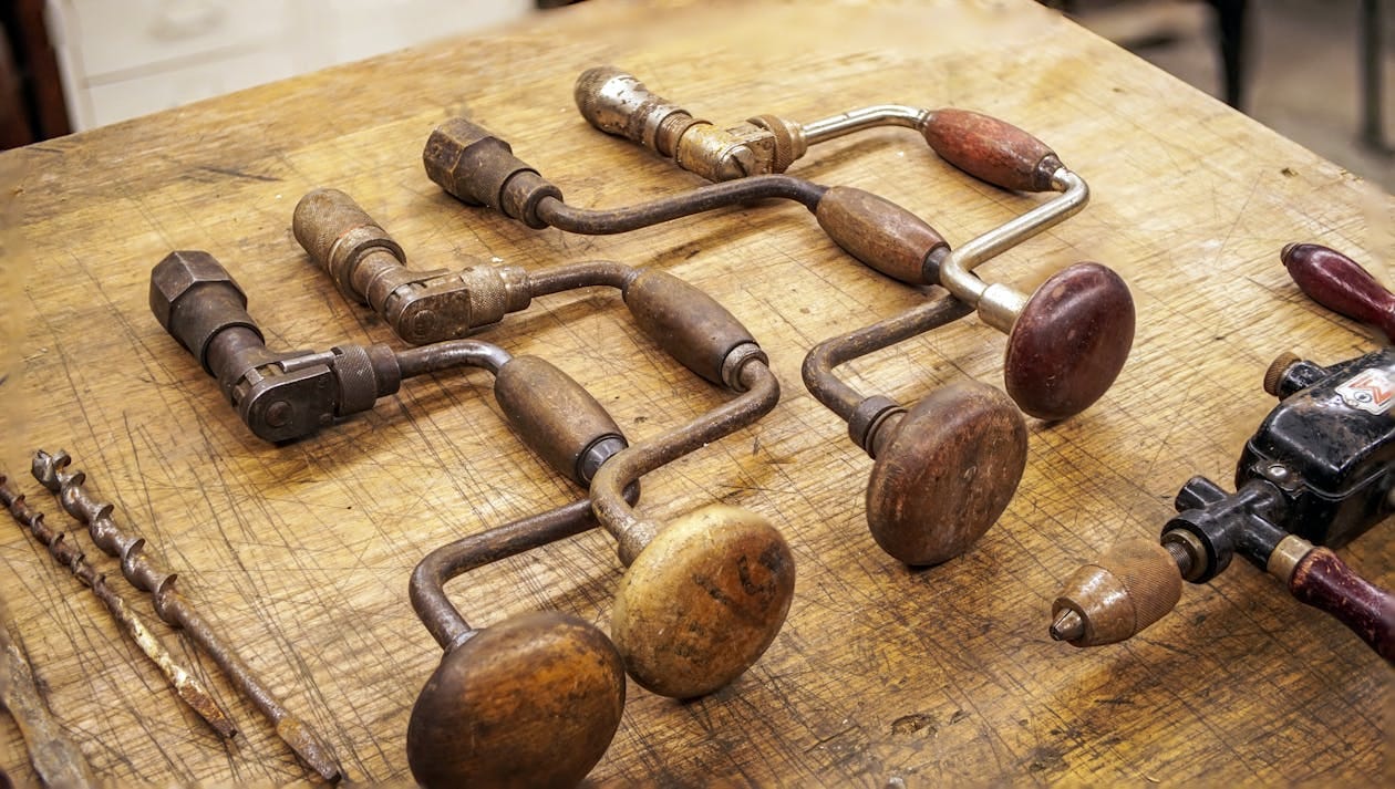 Free Collection of vintage hand drills with wooden handles on a rustic workbench. Stock Photo