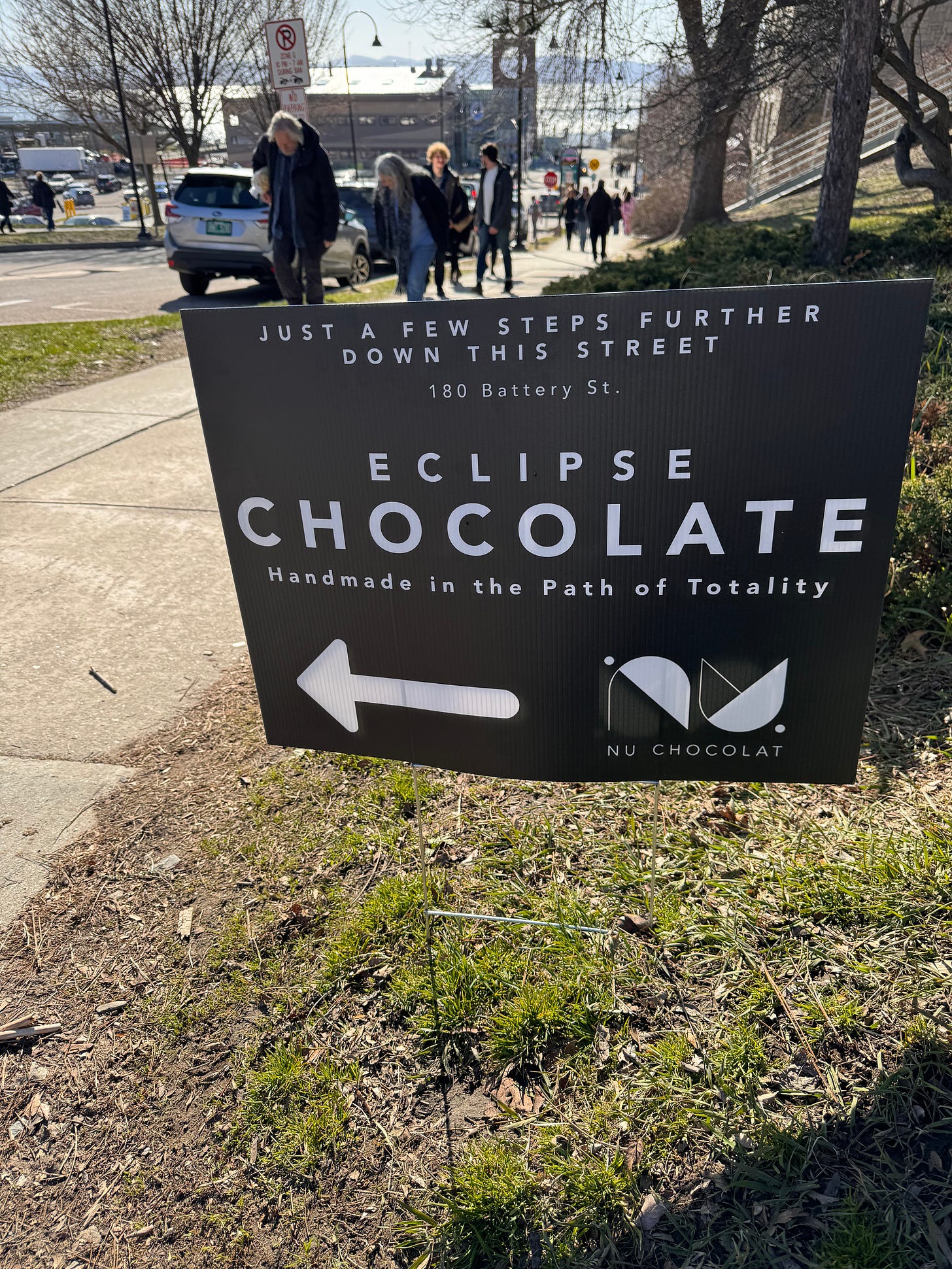 Cardboard sign propped up beside a sidewalk, reading: "Eclipse Chocolate: Handmade in the Path of Totality" (this way)