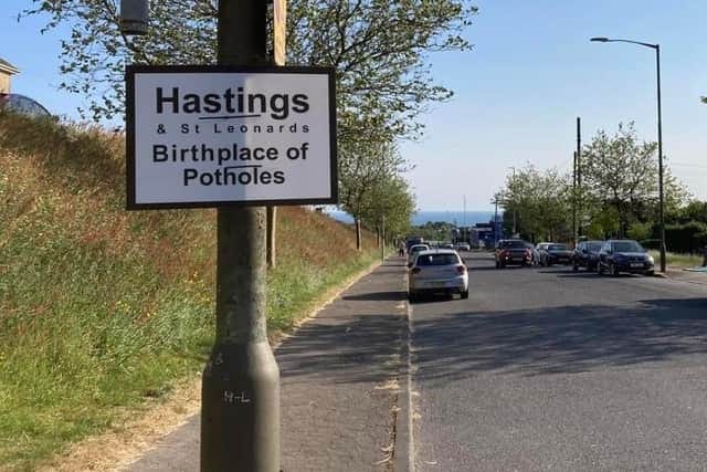 The image shows a lampost in a street in Hastings. It has as sign attached to it that reads: Hastings & St Leonards. Birthplace of Potholes