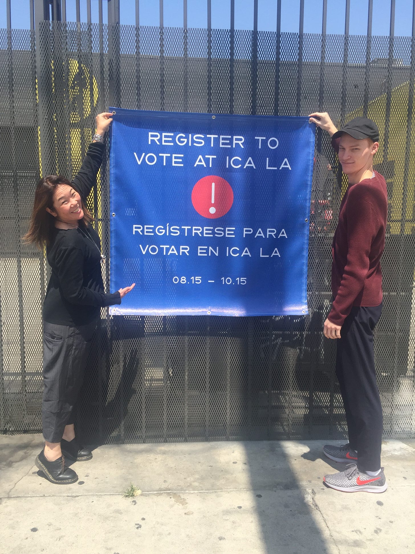 Two people hold up a blue sign in English and Spanish encouraging people to register to vote