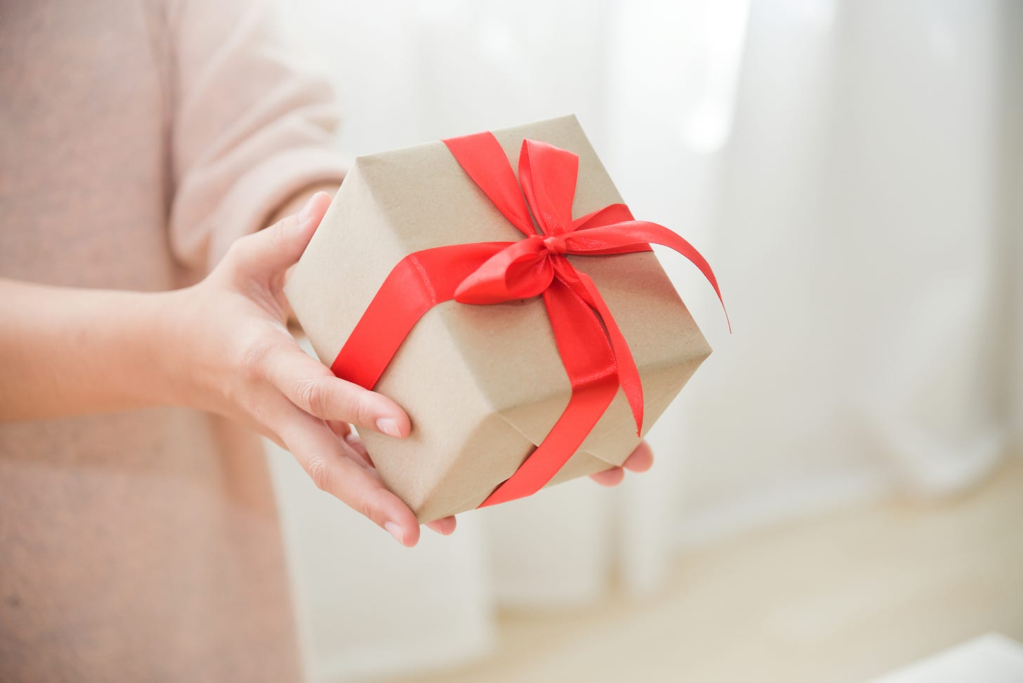 Photograph of a gift wrapped in red ribbon being presented