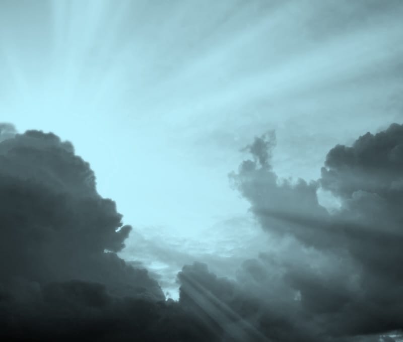 Cloudscape image of dark stormy clouds in blue sky with sun beam. 