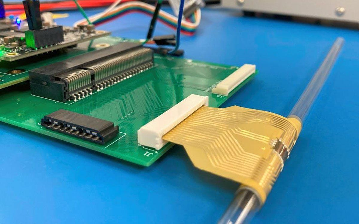 A green circuit board attached to a flexible golden chip wrapped around a thin tube.