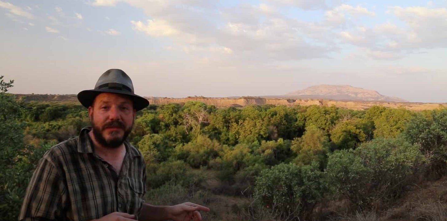 John Hawks in front of a wooded river with badlands in the distance