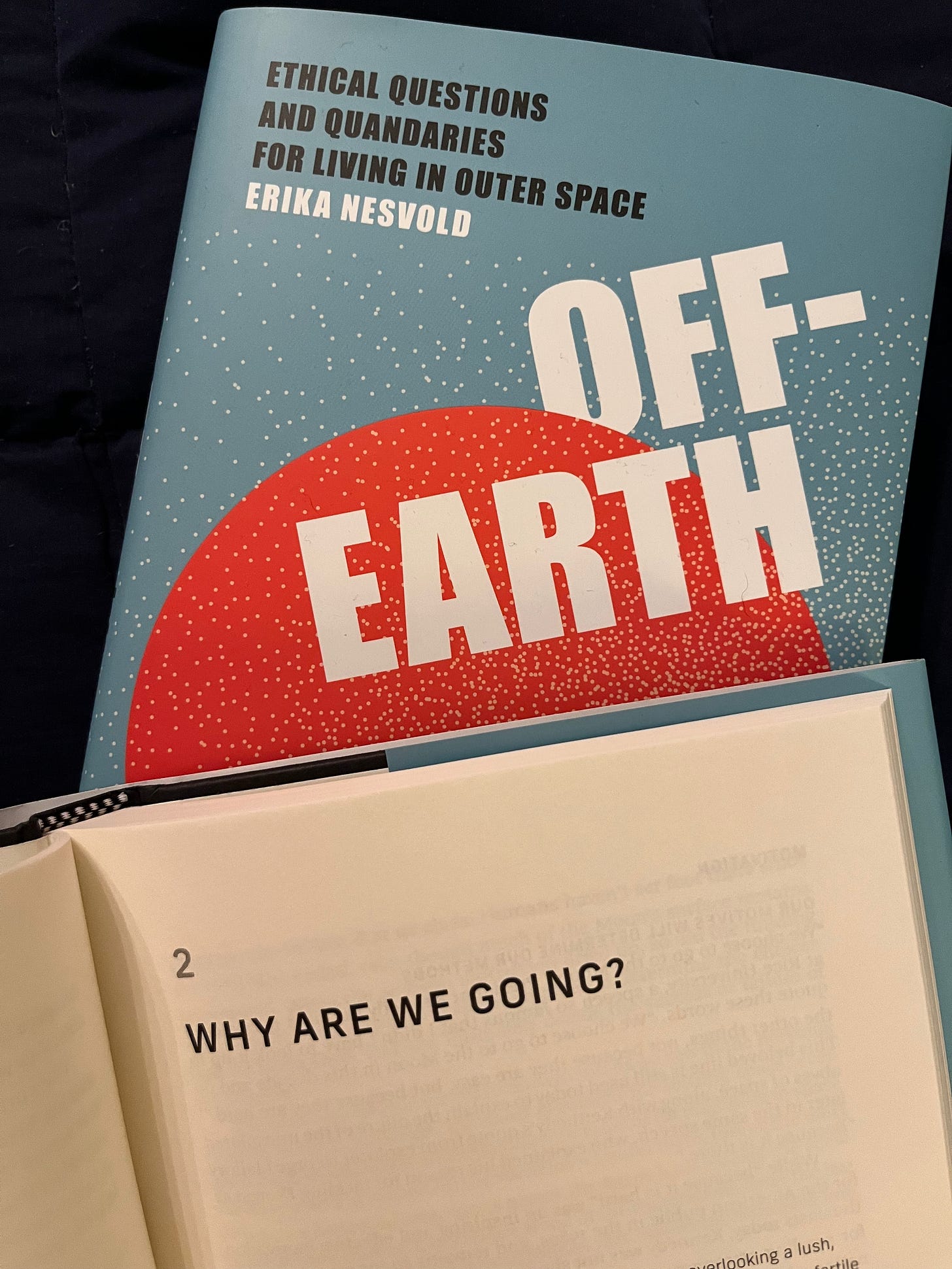 A photo of two copies of Off-Earth. The top is open to Chapter 2: Why Are We Going?. The other is lying underneath the first, showing off the cover.