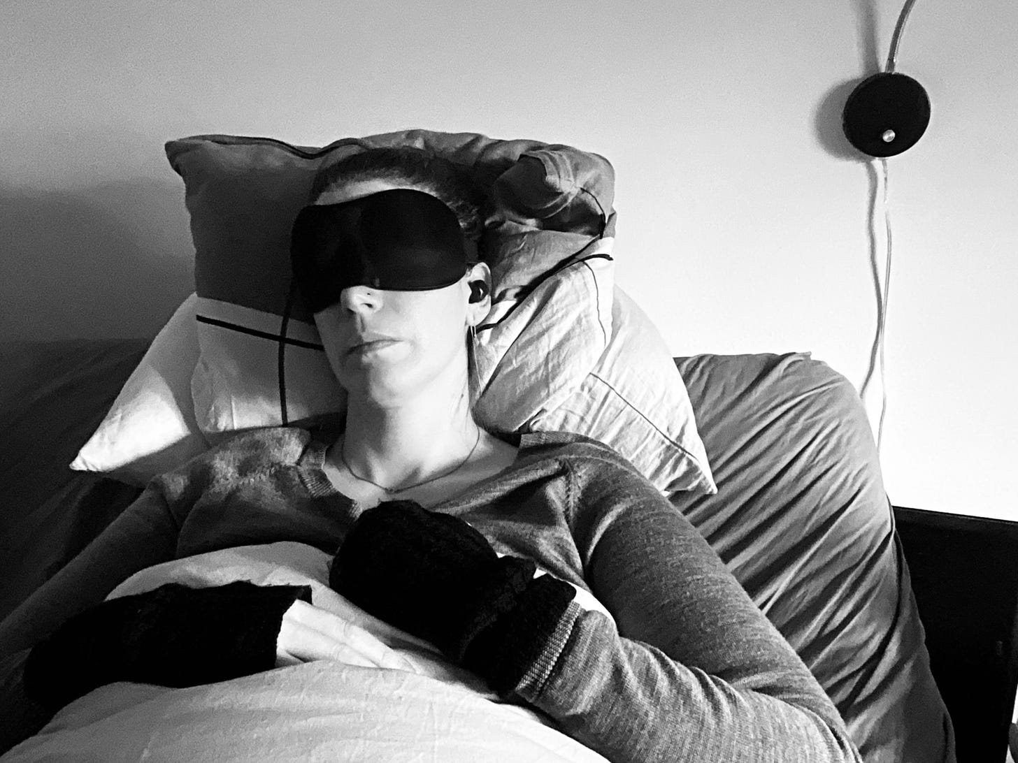 A woman living with severe ME/CFS is resting and wears a sleeping mask to protect her from light as she is light sensitive