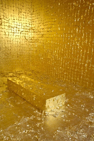 A shiny opulent room made entirely of gold leaf, the walls are made of small squares of gold leaf, in the center of the room is what appears to be a coffin covered entirely in the same gold leaf