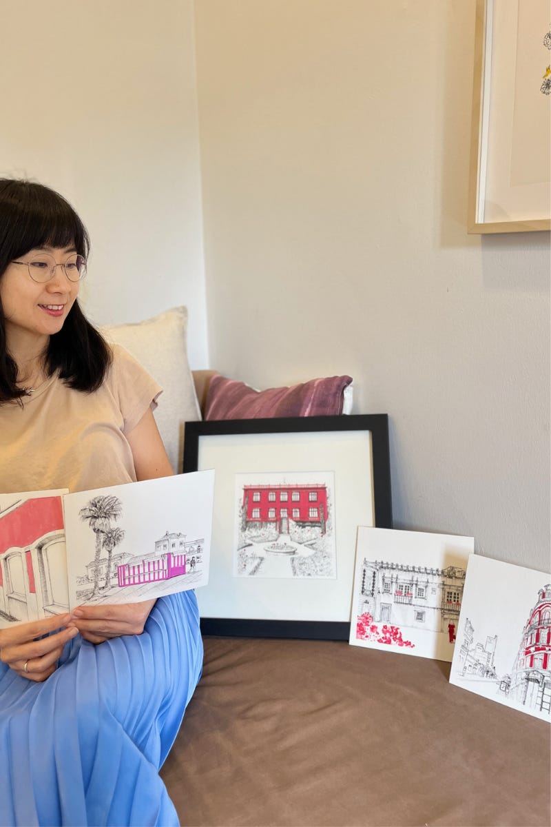 image: photo of a female artist (me again) sitting on a sofa with her five new pieces of line art of Portugal's urban landscape