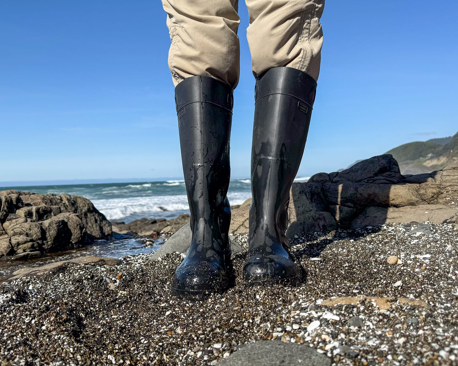 Someone standing in a pair of hightop PVC boots along the coast. 