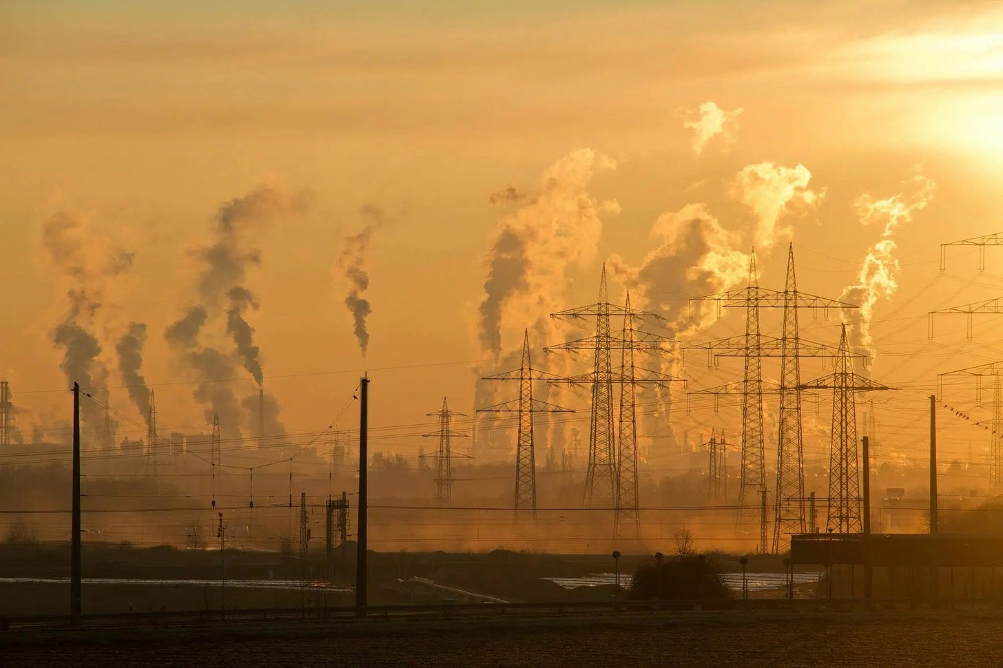 An image of smokestacks and electric towers during sunset.