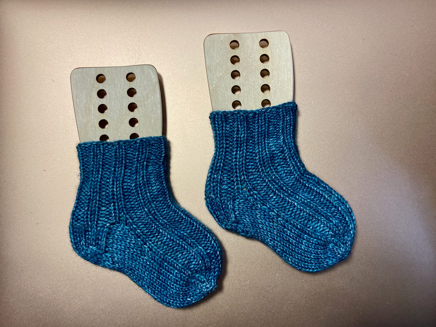 A pair of blue baby socks drying on miniature sock blockers.