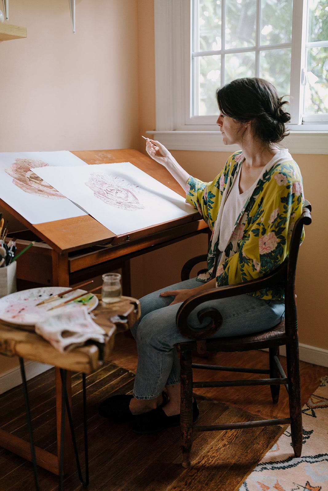 a image of me sitting at my desk, working on a very large painting of radicchio. my watercolors sit on a table to the side, there is a window behind me. 