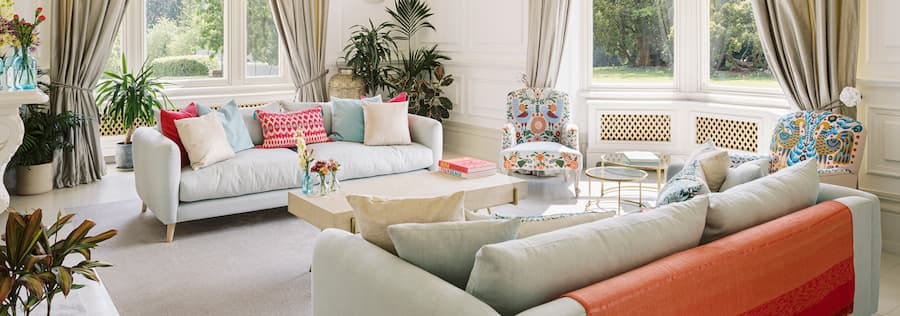 Large bright lounge with two cream sofas positioned opposite each other covered in brightly coloured cushions of turquoise and cerise pink