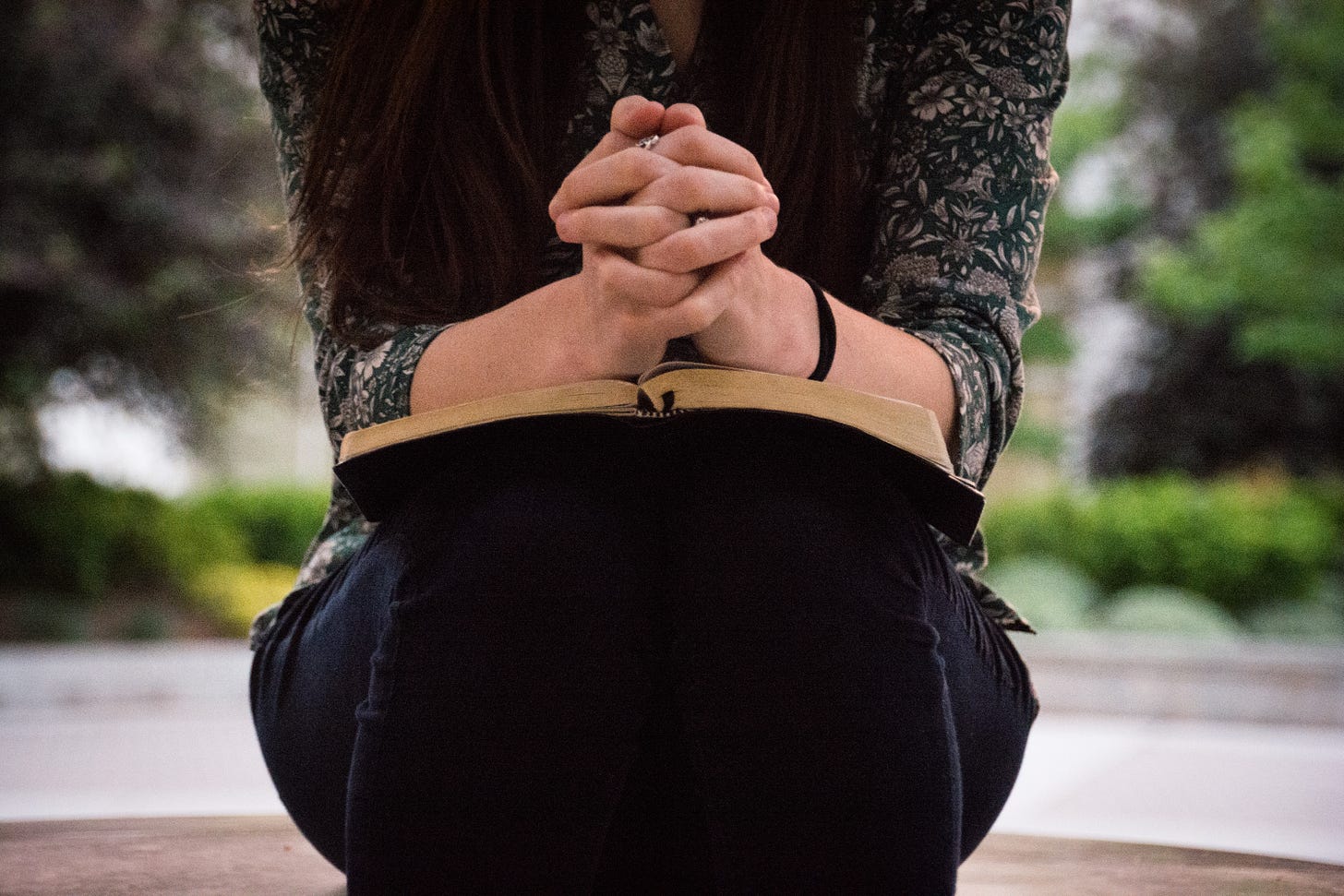 woman praying with clasped hands over Bible in her lap